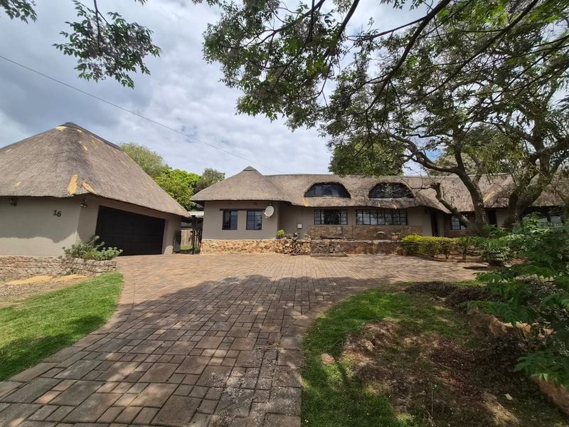 Front exterior view of a house featuring a traditional thatch roof, stone facade detailing, and a spacious paved driveway leading to a garage.