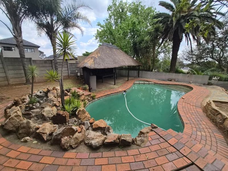 Outdoor pool area featuring a swimming pool, a traditional thatch lapa, and surrounding brick paving with established garden rockery.
