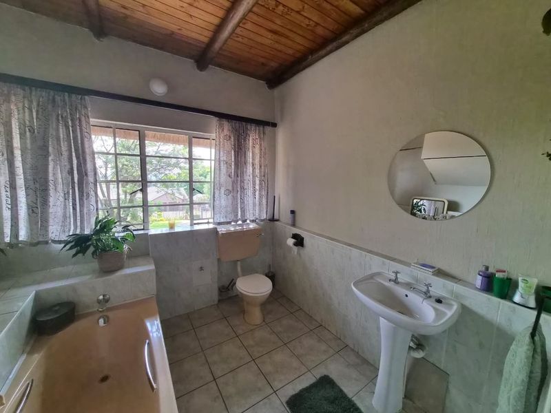 A dated bathroom featuring a pedestal basin, built-in bathtub, toilet, and a timber beam ceiling with tiled wall accents.