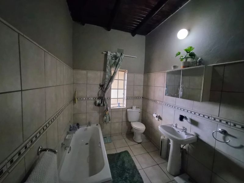 A functional bathroom featuring a pedestal basin, built-in bathtub, toilet, and tiled finishes with exposed timber ceiling beams.