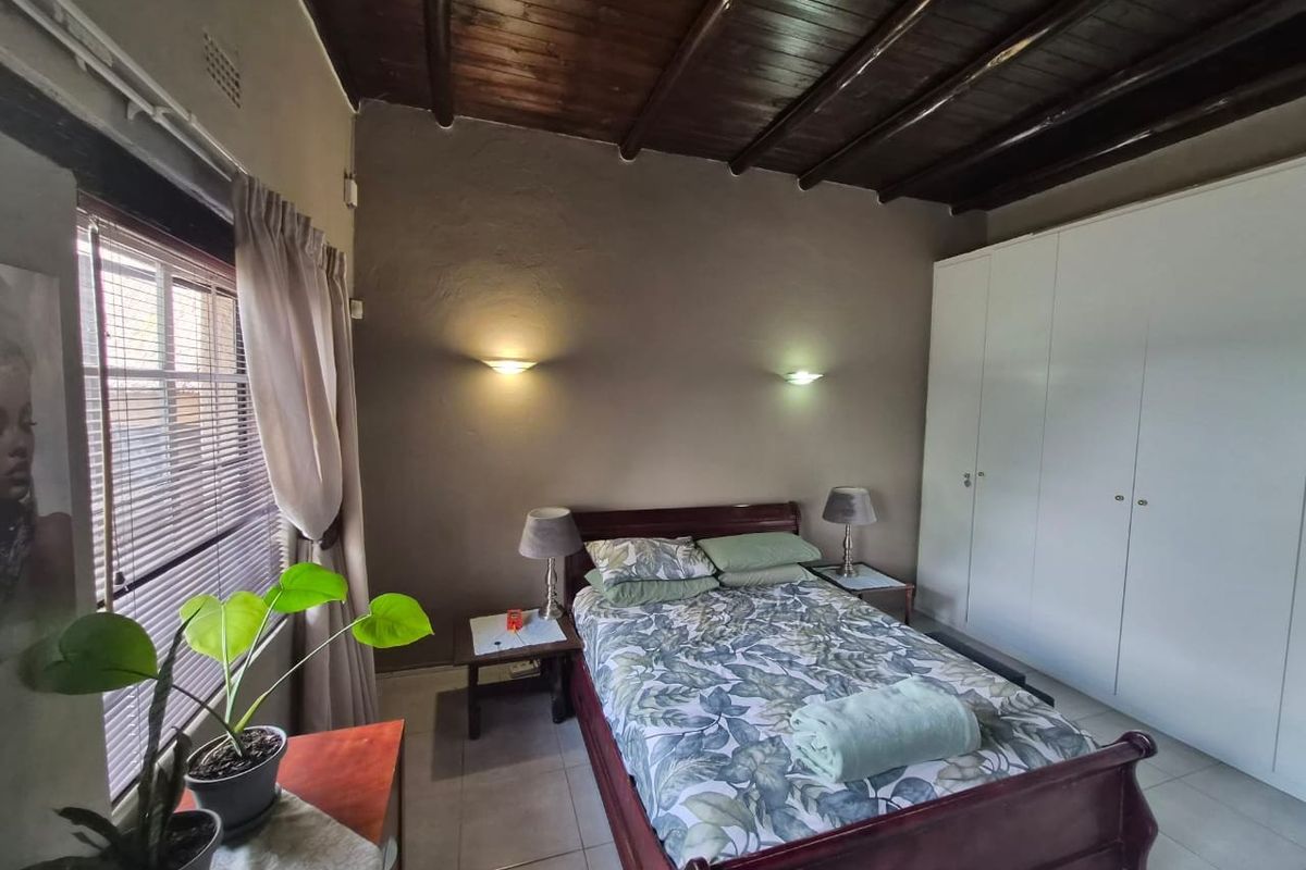 A bedroom featuring a rustic exposed timber beam ceiling, tiled flooring, and built-in cupboards, providing a functional and cozy living space.