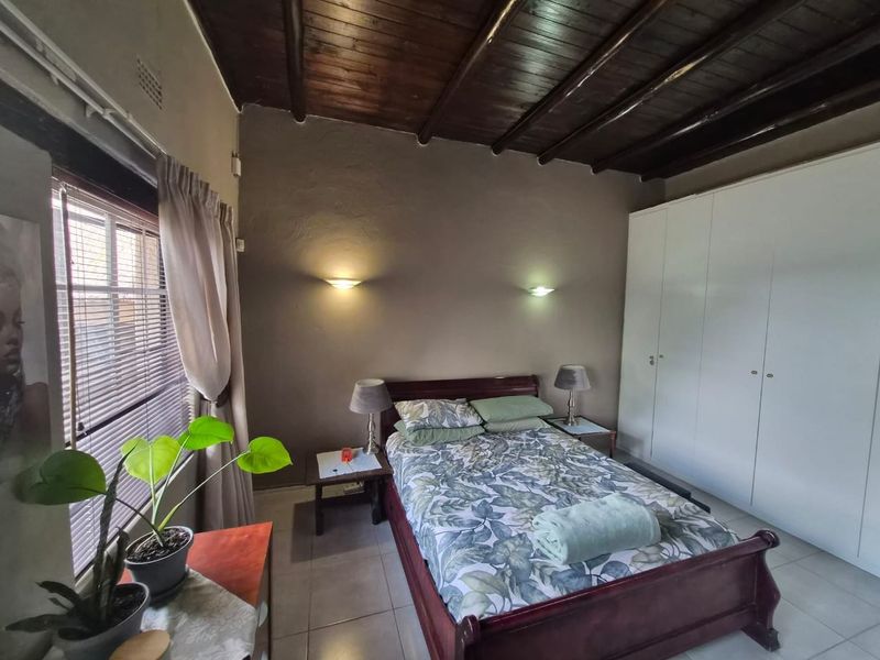 A bedroom featuring a rustic exposed timber beam ceiling, tiled flooring, and built-in cupboards, providing a functional and cozy living space.