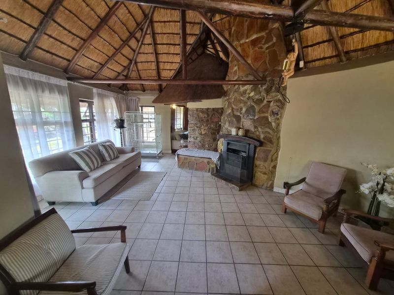 Spacious living room featuring a traditional thatched roof with exposed timber beams and a prominent stone fireplace.