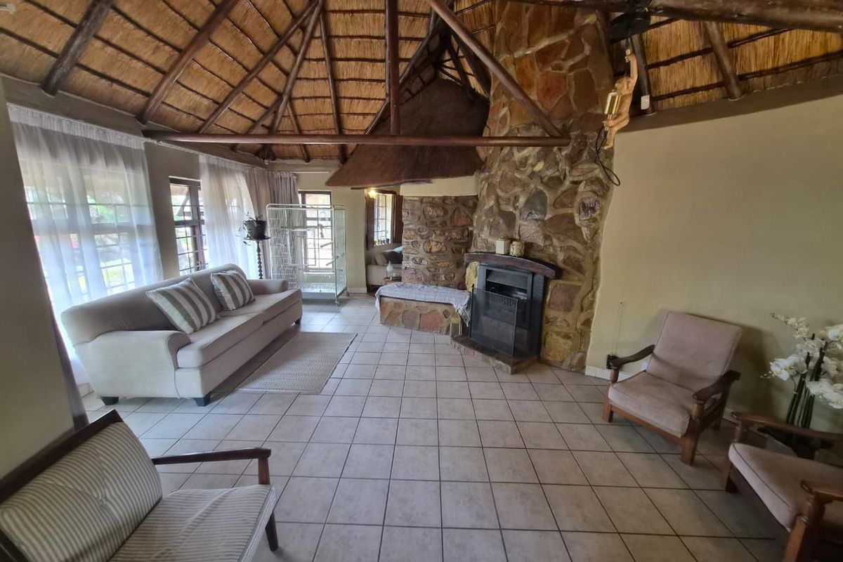 Spacious living room featuring a traditional thatched roof with exposed timber beams and a prominent stone fireplace.