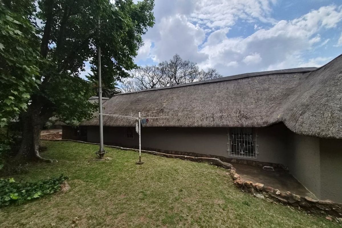 Rear view of a house featuring a traditional thatched roof, security bars on windows, and a surrounding garden area.