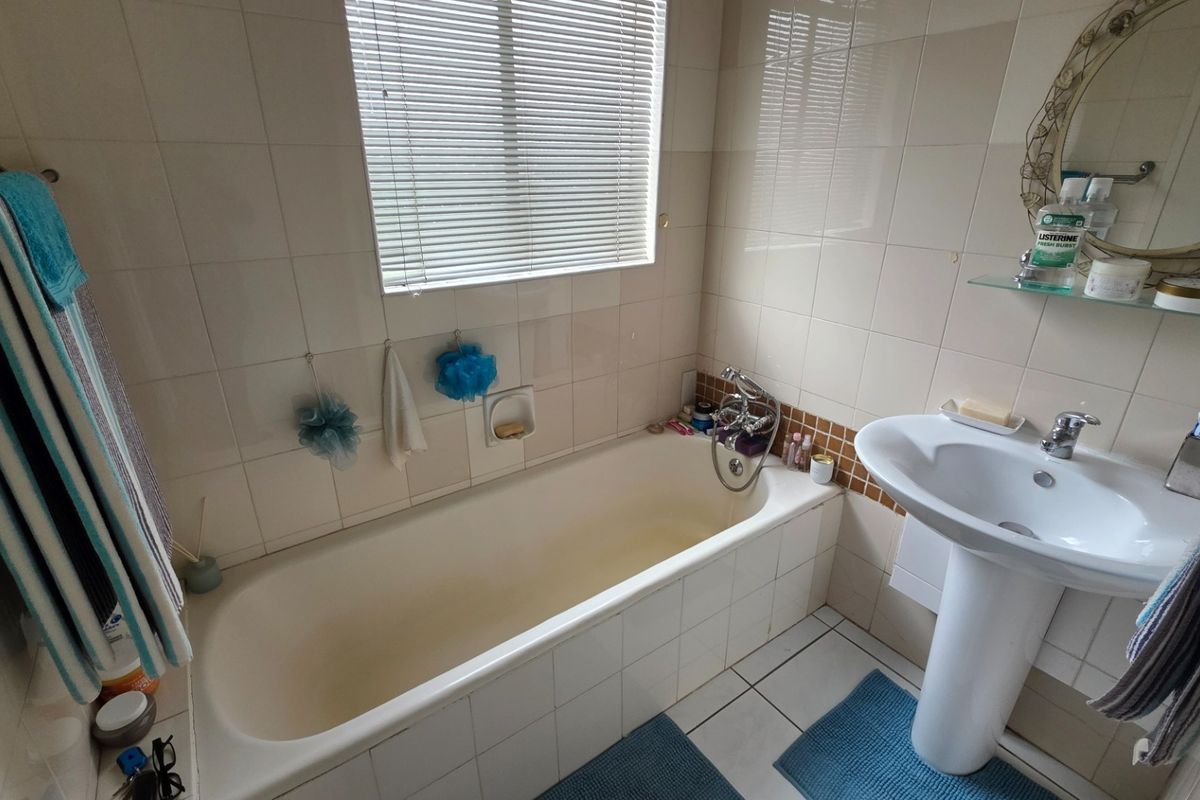 A functional bathroom featuring a pedestal basin, bathtub with mixer tap, and neutral wall tiling with a window for natural light.