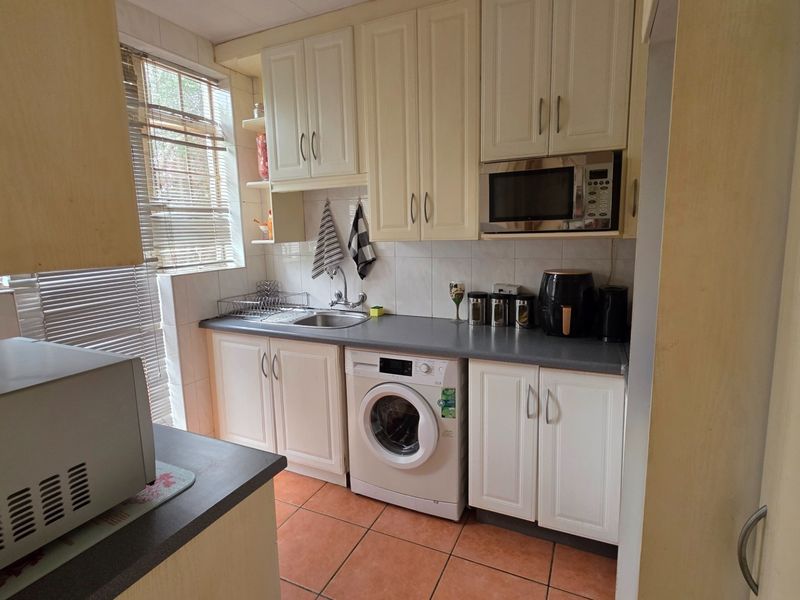 A functional scullery featuring built-in cabinetry, laminate countertops, a stainless steel sink, and space for a washing machine.