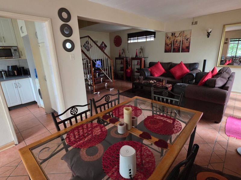 Open-plan living and dining area featuring tiled flooring, a staircase with metal railing, and an adjacent kitchen with built-in cabinetry.