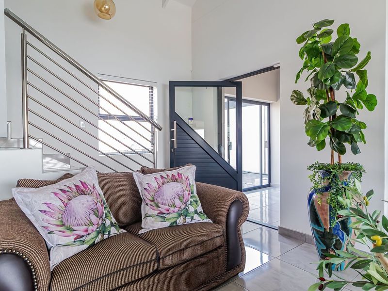 Bright living area featuring modern tiled flooring, a contemporary stainless steel staircase railing, and a stylish glass-paneled door leading to an adjacent space.