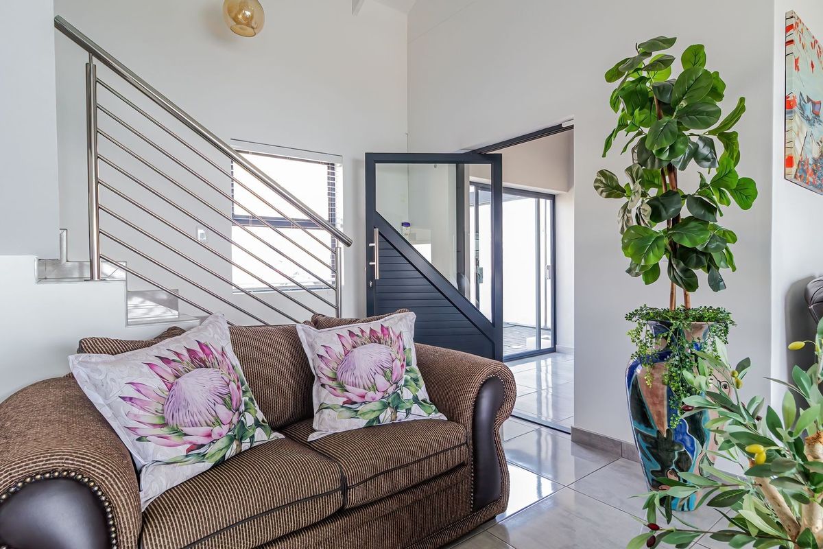 Bright living area featuring modern tiled flooring, a contemporary stainless steel staircase railing, and a stylish glass-paneled door leading to an adjacent space.