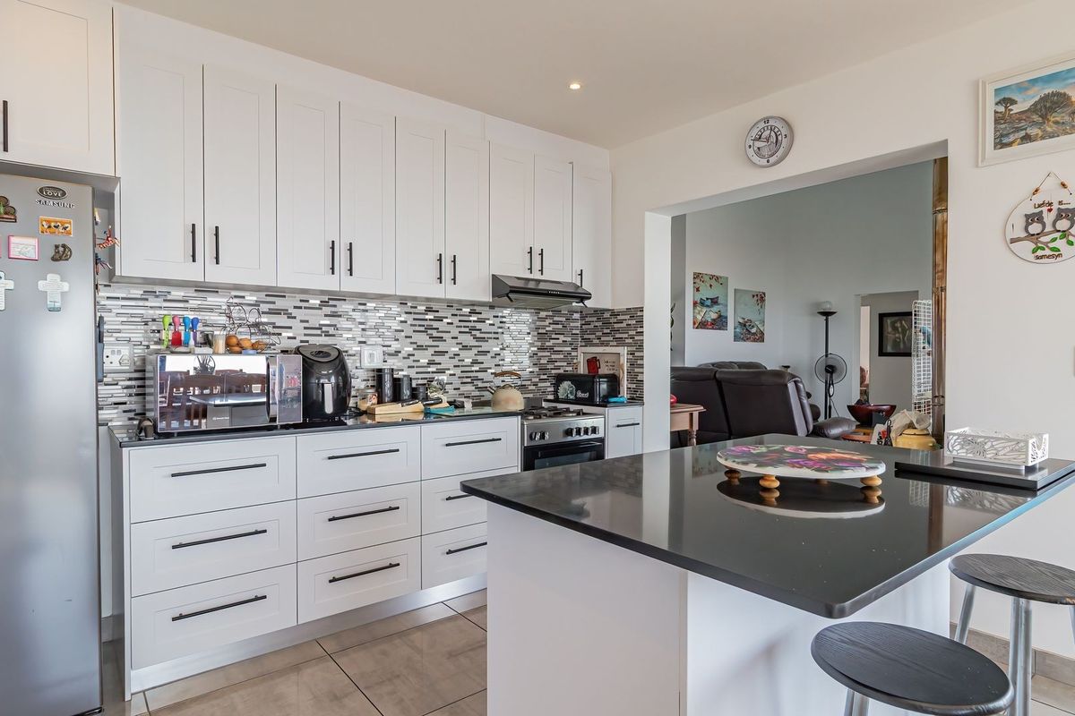 Modern kitchen featuring white shaker cabinetry, black granite countertops, a mosaic tile backsplash, and a functional kitchen island, seamlessly flowing into the living area.