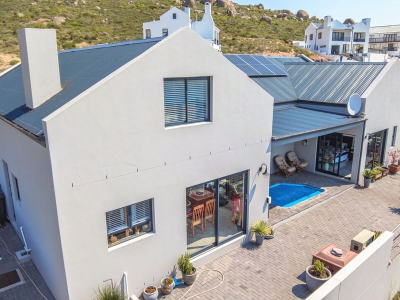Aerial view of a modern house featuring a metal roof with solar panels, a paved patio area, and a small plunge pool.