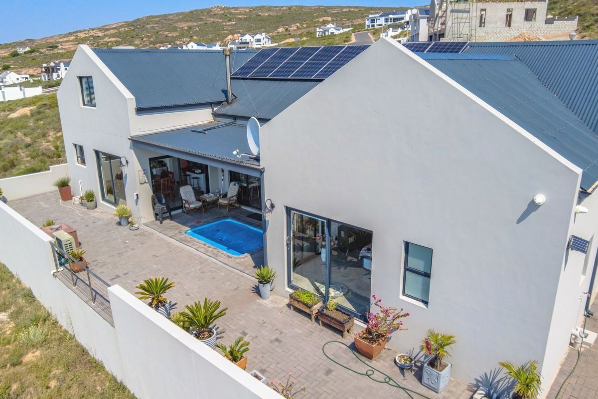Aerial view of a modern home featuring a metal roof with solar panels, a paved patio area, and a private swimming pool.