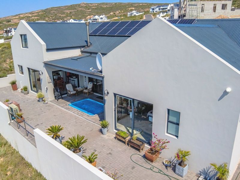 Aerial view of a modern home featuring a metal roof with solar panels, a paved patio area, and a private swimming pool.