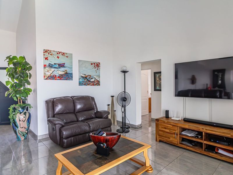 A bright living room featuring large format floor tiles, high vaulted ceilings, and a neutral wall finish, providing a spacious and comfortable atmosphere.