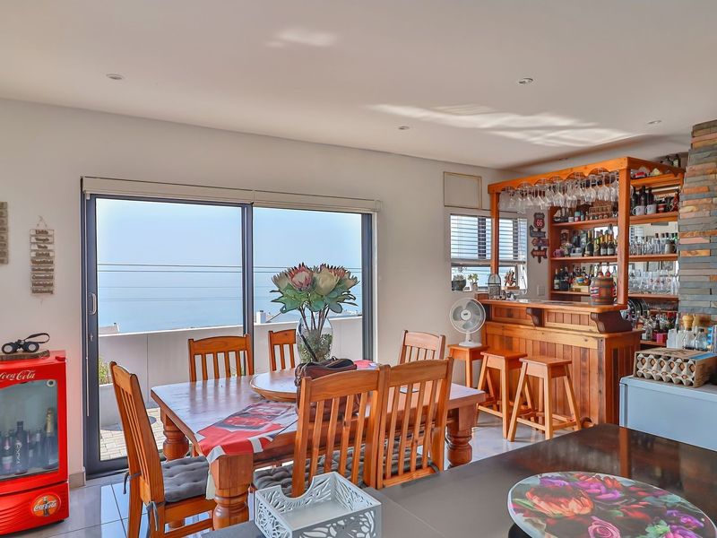 Open-plan living and dining area featuring a built-in timber bar, stone feature wall, and sliding glass doors with ocean views.
