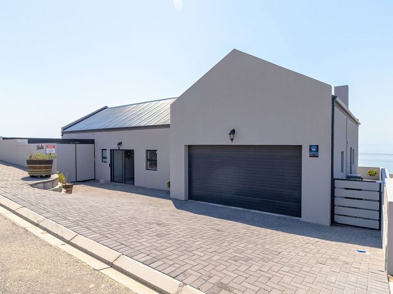 Modern single-story residence featuring a paved driveway, automated garage, and clean architectural lines with a contemporary grey finish.