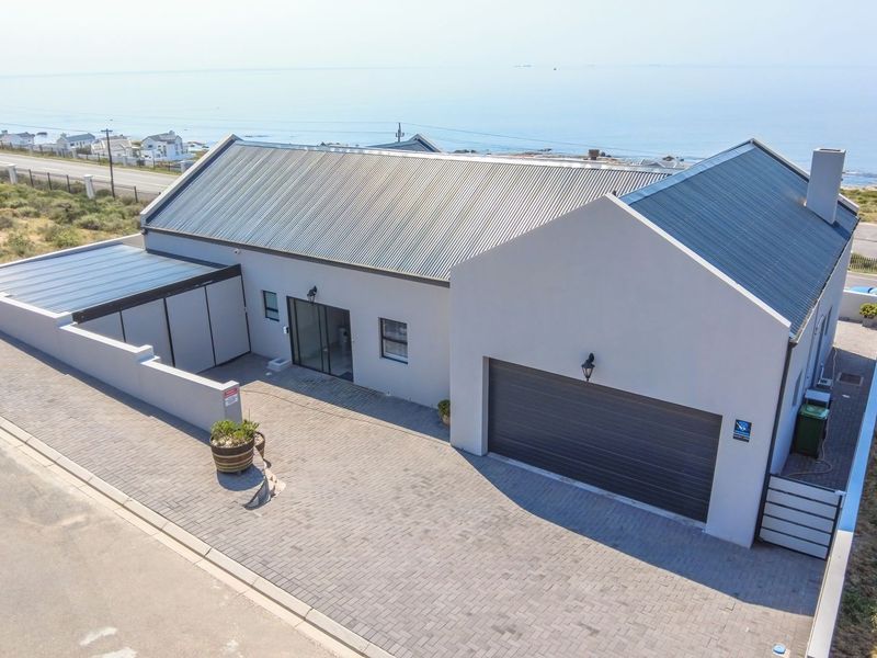 Aerial view of a modern coastal home featuring a corrugated metal roof, paved driveway, and attached double garage with ocean views.