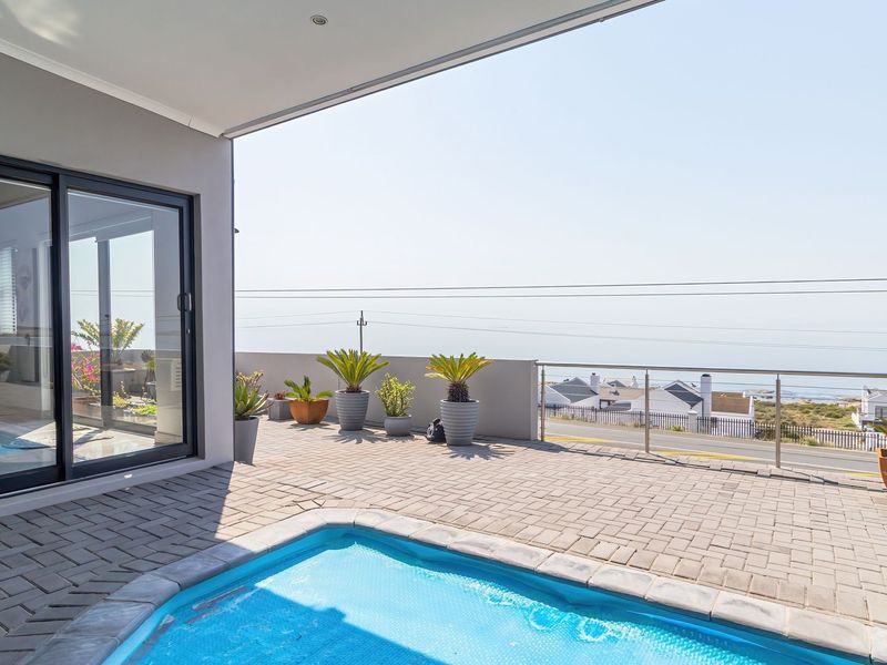 Spacious covered patio featuring a swimming pool, paved flooring, and a modern stainless steel balustrade with coastal views.