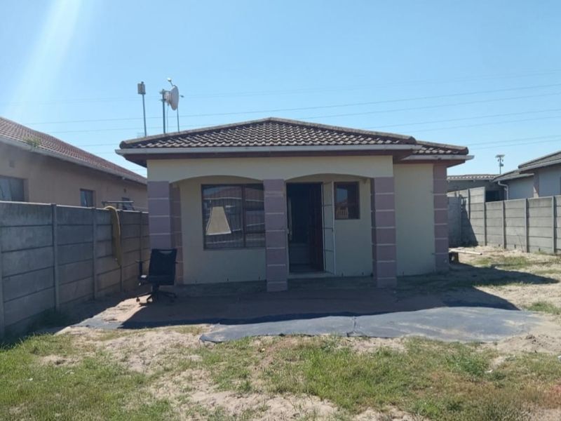 Rear view of a townhouse featuring a covered patio, tiled roof, and a large, unlandscaped yard enclosed by concrete boundary walls.