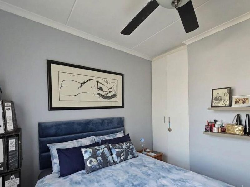 A well-maintained bedroom featuring a built-in wardrobe, ceiling fan, and neutral wall finishes.