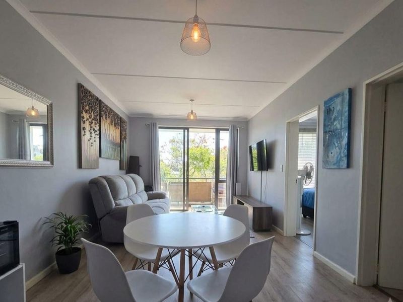Open plan living and dining area featuring laminate flooring, neutral wall tones, and a sliding glass door leading to an outdoor balcony.