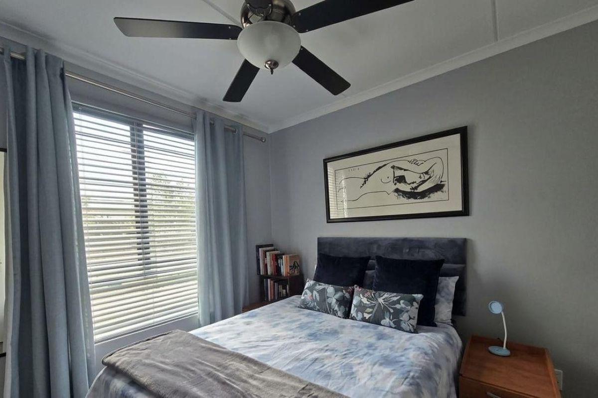 A well-maintained bedroom featuring a ceiling fan, neutral wall finishes, and large windows with venetian blinds for natural light control.