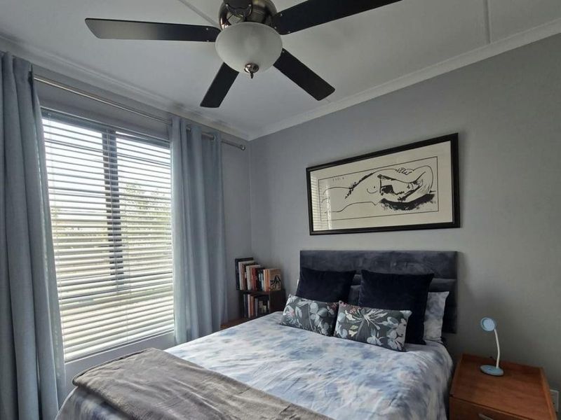 A well-maintained bedroom featuring a ceiling fan, neutral wall finishes, and large windows with venetian blinds for natural light control.