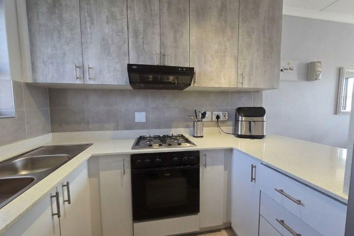 Modern kitchen featuring stone countertops, built-in gas hob, oven, extractor fan, and ample cabinetry with a neutral tiled backsplash.