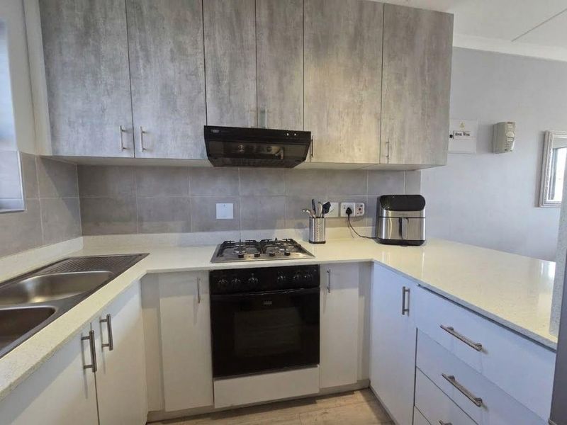 Modern kitchen featuring stone countertops, built-in gas hob, oven, extractor fan, and ample cabinetry with a neutral tiled backsplash.
