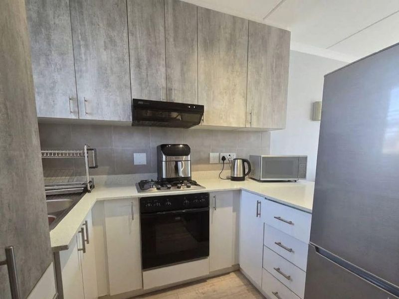 Modern kitchen featuring light grey wood-look cabinetry, stone countertops, gas hob, electric oven, and a tiled backsplash.