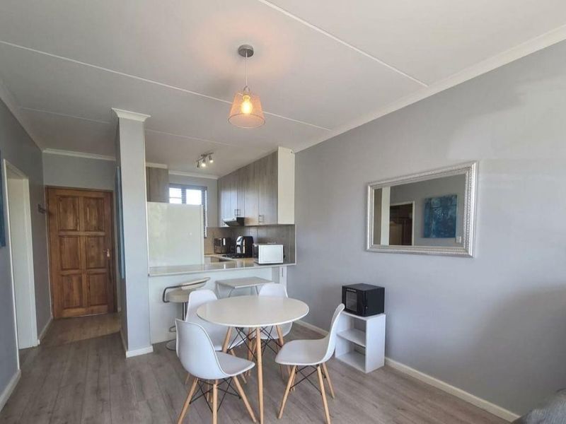 Open-plan living and dining area featuring laminate flooring, a breakfast bar, and a functional kitchen with built-in cabinetry.