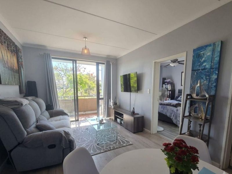 Open plan living area featuring laminate flooring and a sliding glass door leading to a balcony, with direct access to an adjacent bedroom.