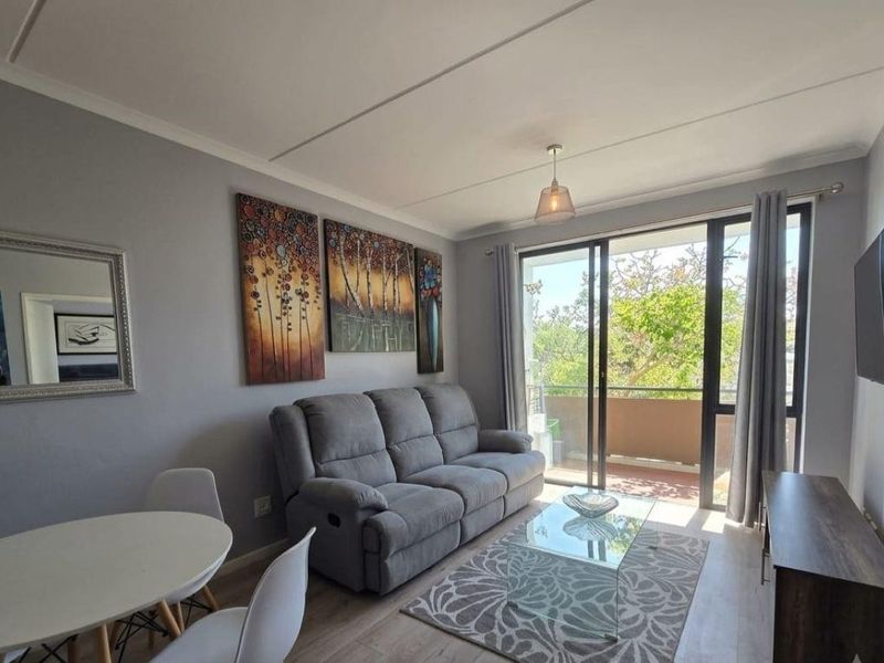 A well-lit living room featuring laminate flooring and large sliding glass doors that provide direct access to an outdoor balcony.