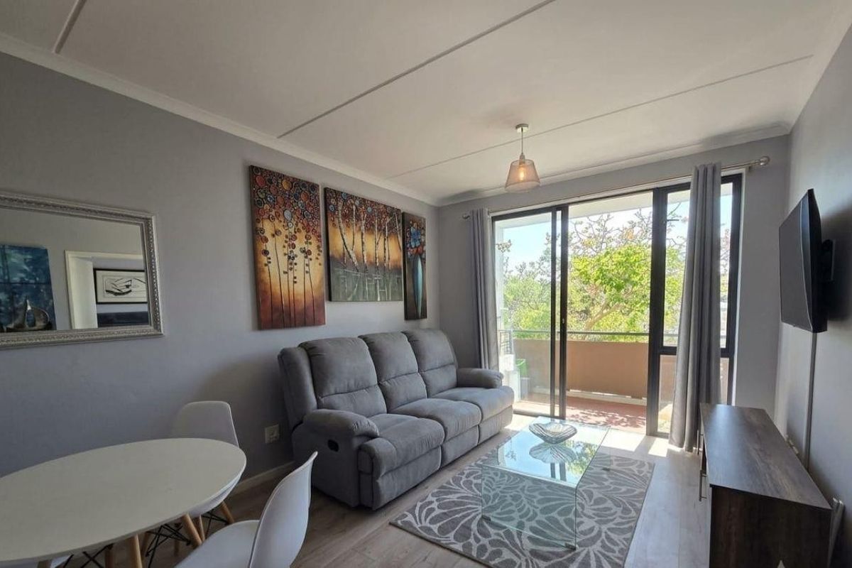 A well-lit living room featuring laminate flooring and large sliding glass doors that provide direct access to an outdoor balcony.