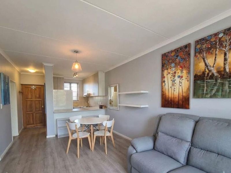 An open-plan living and dining area featuring laminate flooring, neutral walls, and a functional kitchen with built-in cabinetry and a breakfast counter.