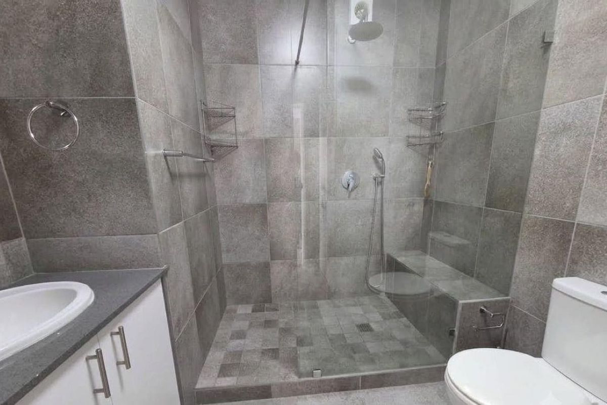 Modern bathroom featuring a spacious walk-in shower with a built-in bench, glass screen, vanity cabinet with countertop basin, and neutral grey tiling.