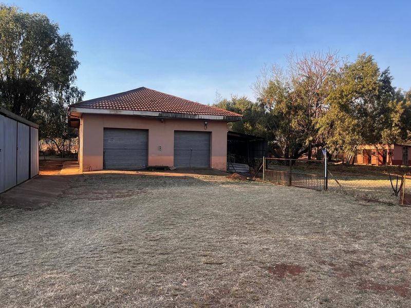 A detached double garage structure with roller doors, situated on a large residential plot with mature trees and perimeter fencing.