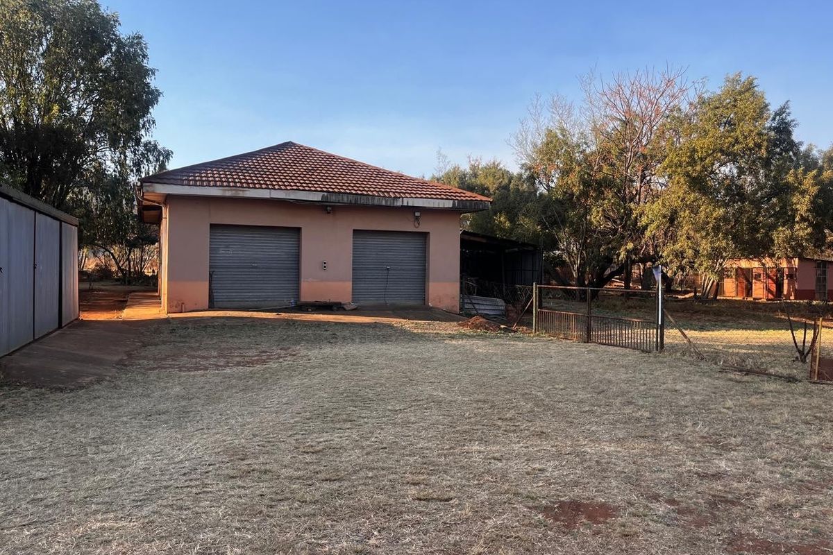 A detached double garage structure with roller doors, situated on a large residential plot with mature trees and perimeter fencing.