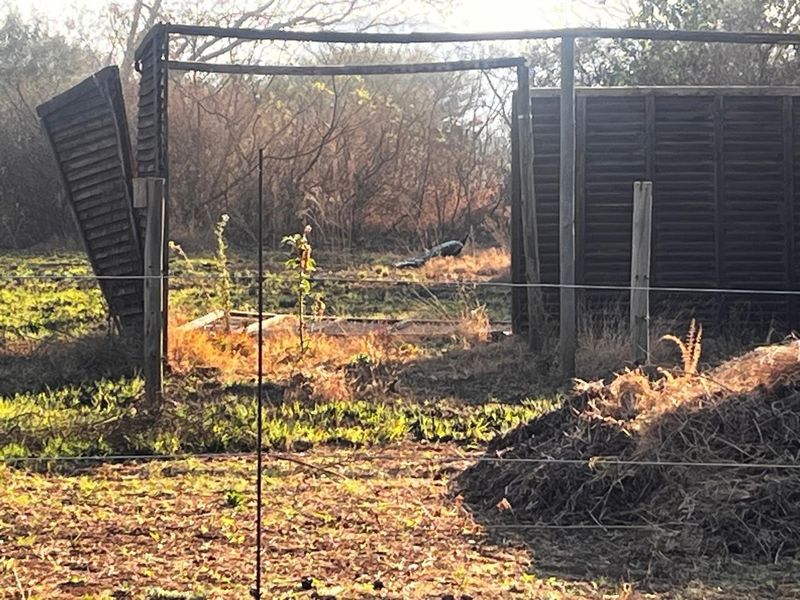 A view of a vacant residential plot featuring damaged timber fencing and overgrown vegetation, indicating a need for site clearing and maintenance.