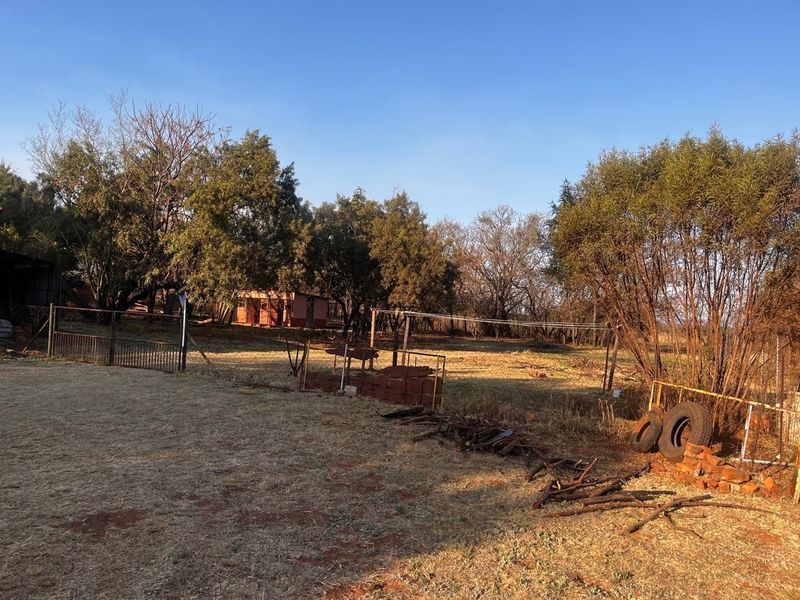 A large, open residential plot featuring mature trees, wire fencing, and a metal gate, offering significant potential for development or landscaping.