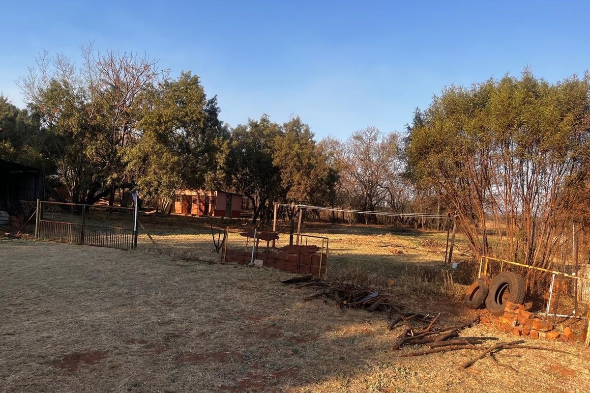 A large, open residential plot featuring mature trees, wire fencing, and a metal gate, offering significant potential for development or landscaping.
