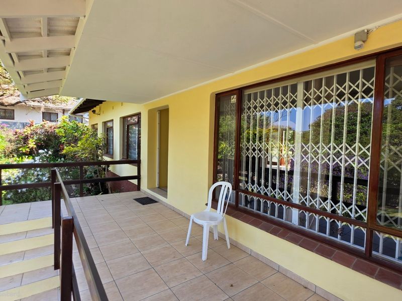 A covered outdoor patio featuring tiled flooring, timber railings, and security gates, providing a functional space overlooking the garden area.