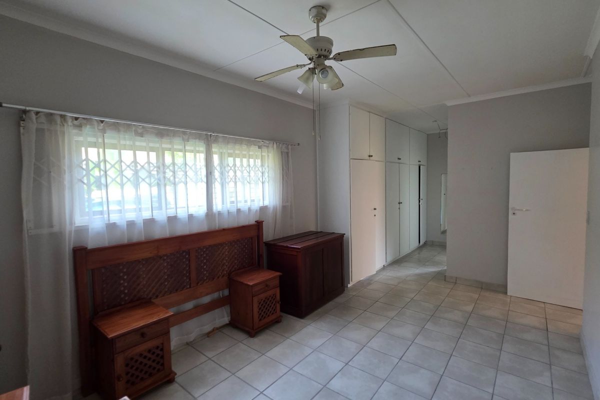 A bedroom featuring tiled flooring, built-in cupboards, and a ceiling fan, with security gates installed on the windows.