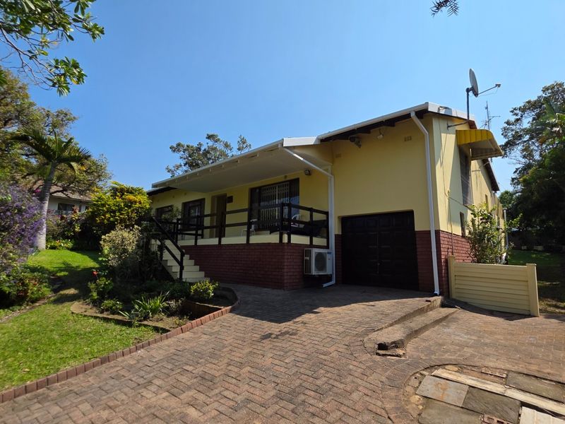Front view of a single-story house featuring a brick driveway, covered patio, and attached garage, set within a landscaped garden.