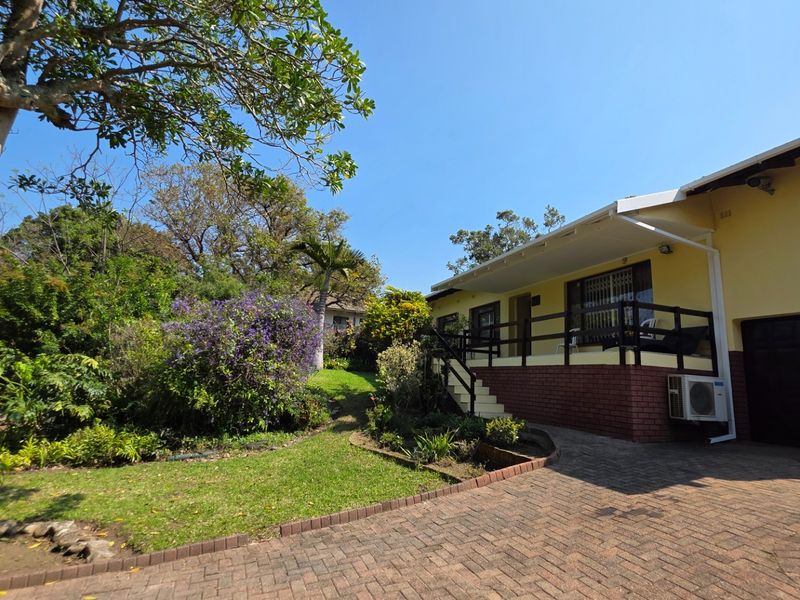 A well-maintained front exterior featuring a paved driveway, a raised patio with timber railings, and a lush, established garden.