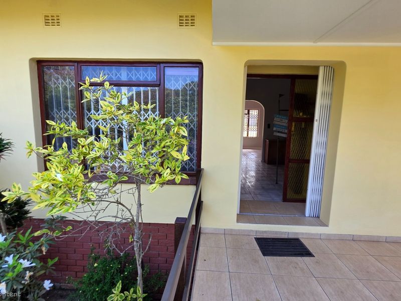 A covered patio area featuring tiled flooring, brick base detailing, and security gates leading into the home's interior.