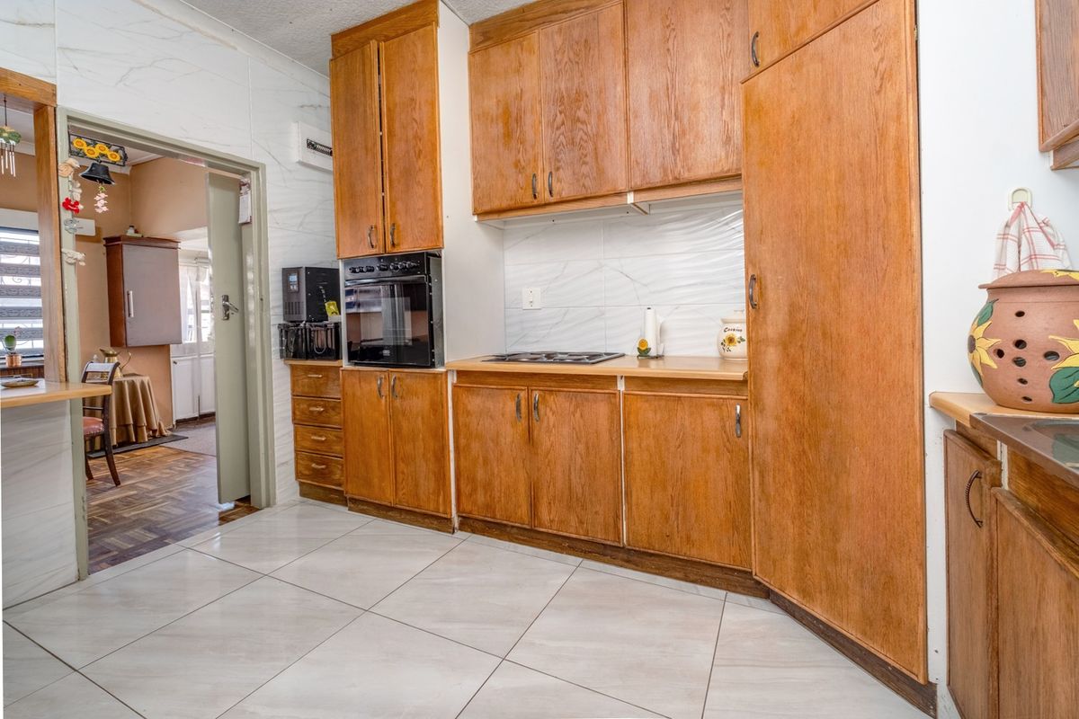 A functional kitchen featuring wooden cabinetry, built-in oven, hob, and tiled flooring, offering a classic layout with potential for modern updates.