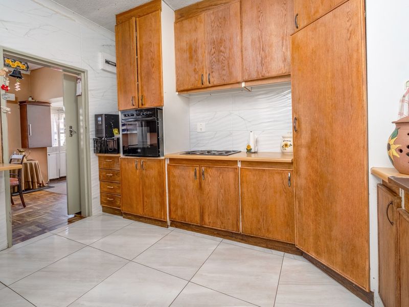 A functional kitchen featuring wooden cabinetry, built-in oven, hob, and tiled flooring, offering a classic layout with potential for modern updates.