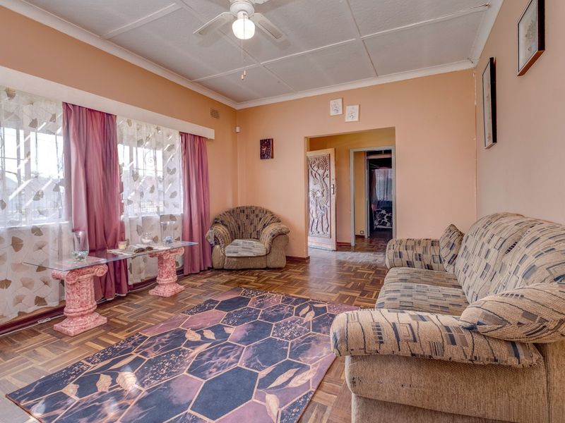 A living room featuring parquet flooring, a ceiling fan, and a decorative carved wooden door, with large windows fitted with security bars.